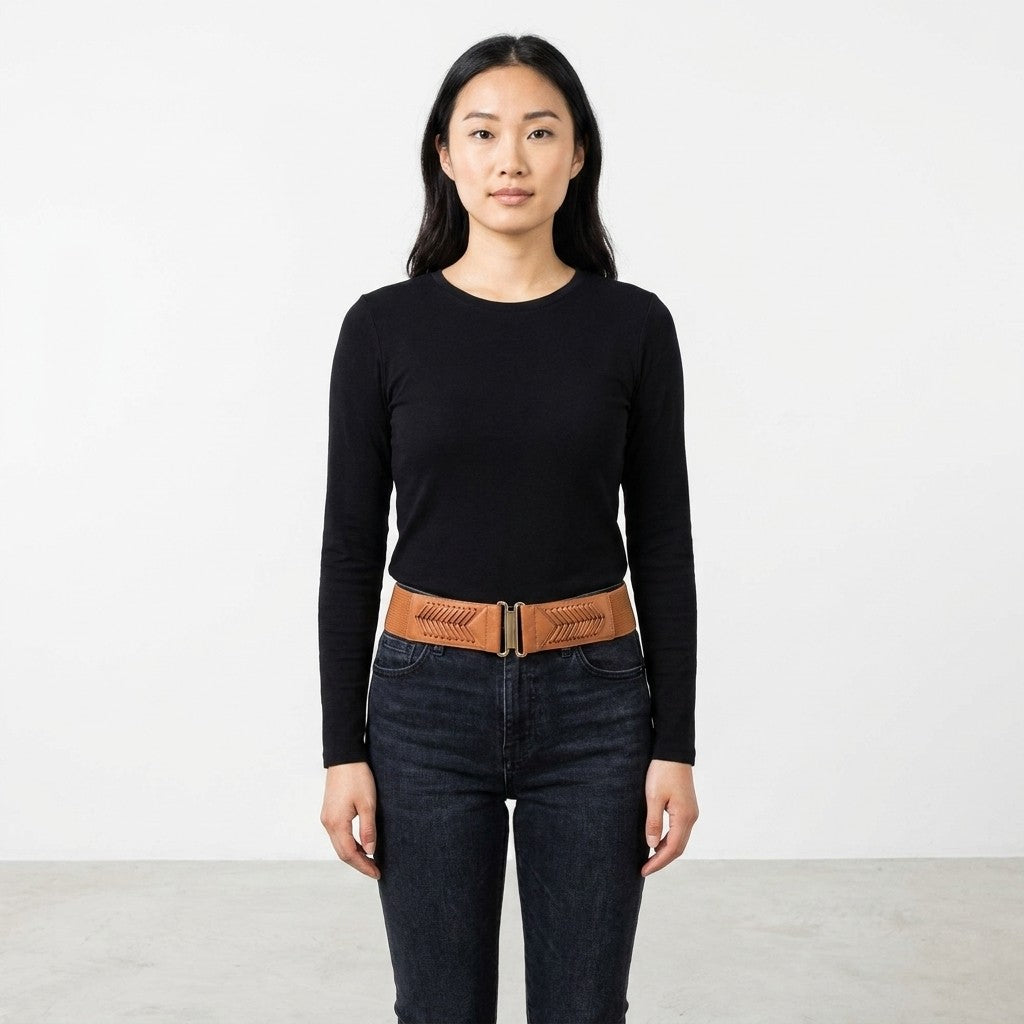 Woman in black top and jeans, brown belt, standing against a white background.