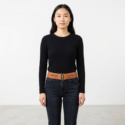 Woman in black top and jeans, brown belt, standing against a white background.