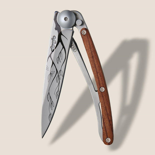 Folding knife with a wooden handle and leaf engravings on the blade.