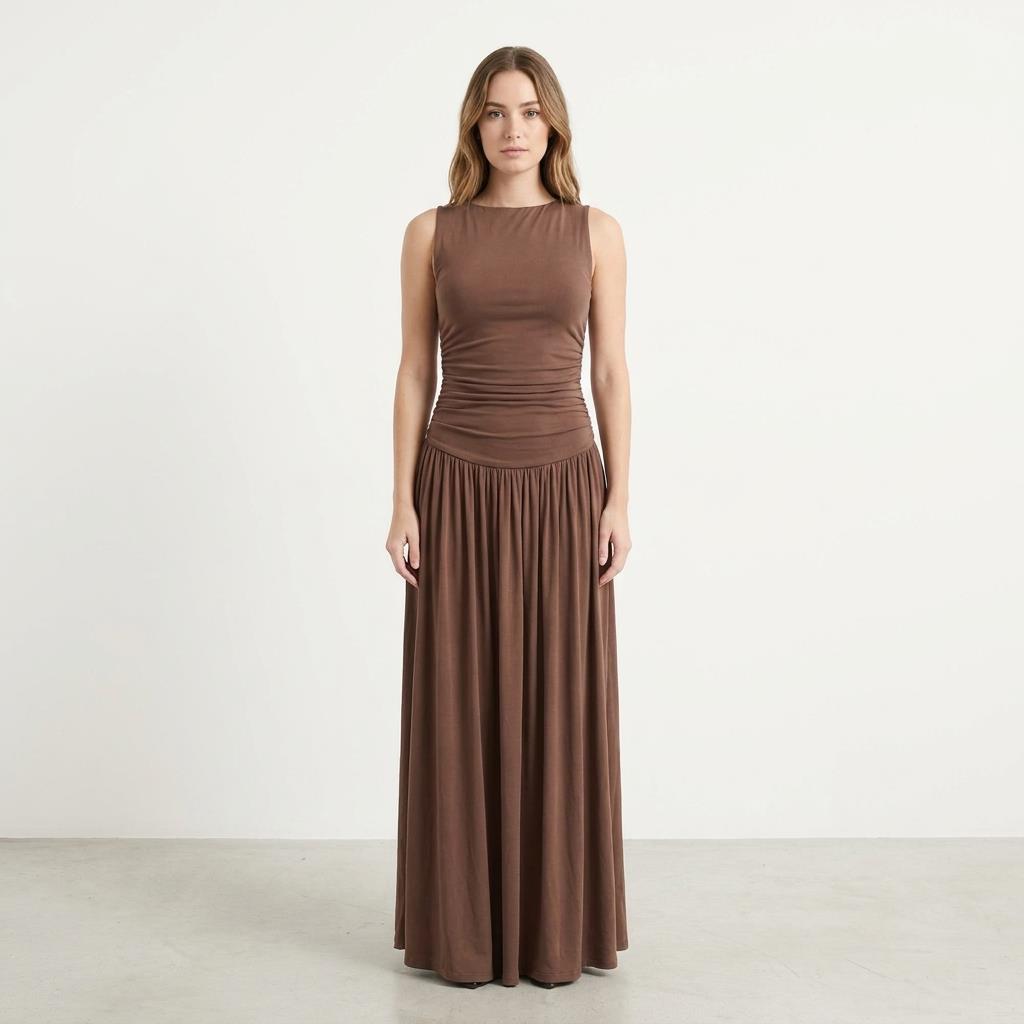 Woman in a long brown dress stands against a plain white background.