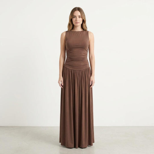 Woman in a long brown dress stands against a plain white background.