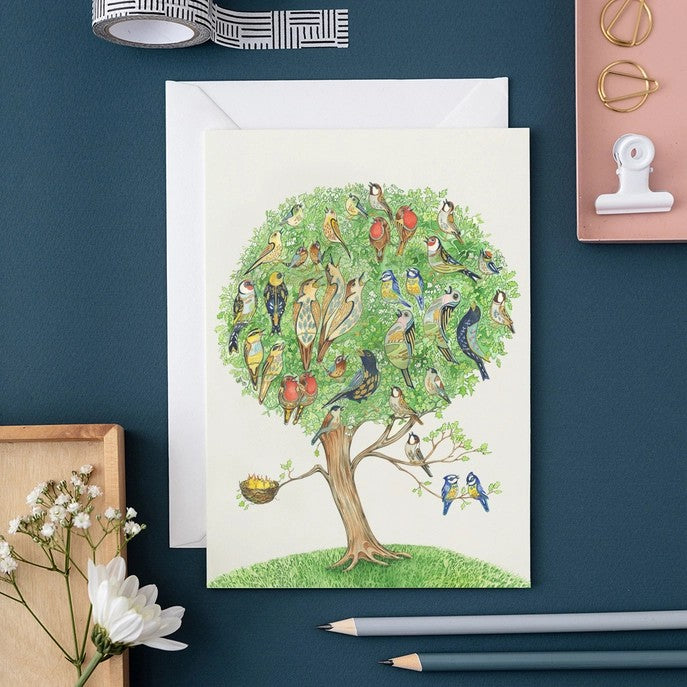 Illustrated card with colorful birds in a tree, surrounded by stationery items.