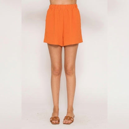 Person wearing orange shorts, brown sandals; standing on white background.