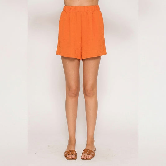 Person wearing orange shorts, brown sandals; standing on white background.