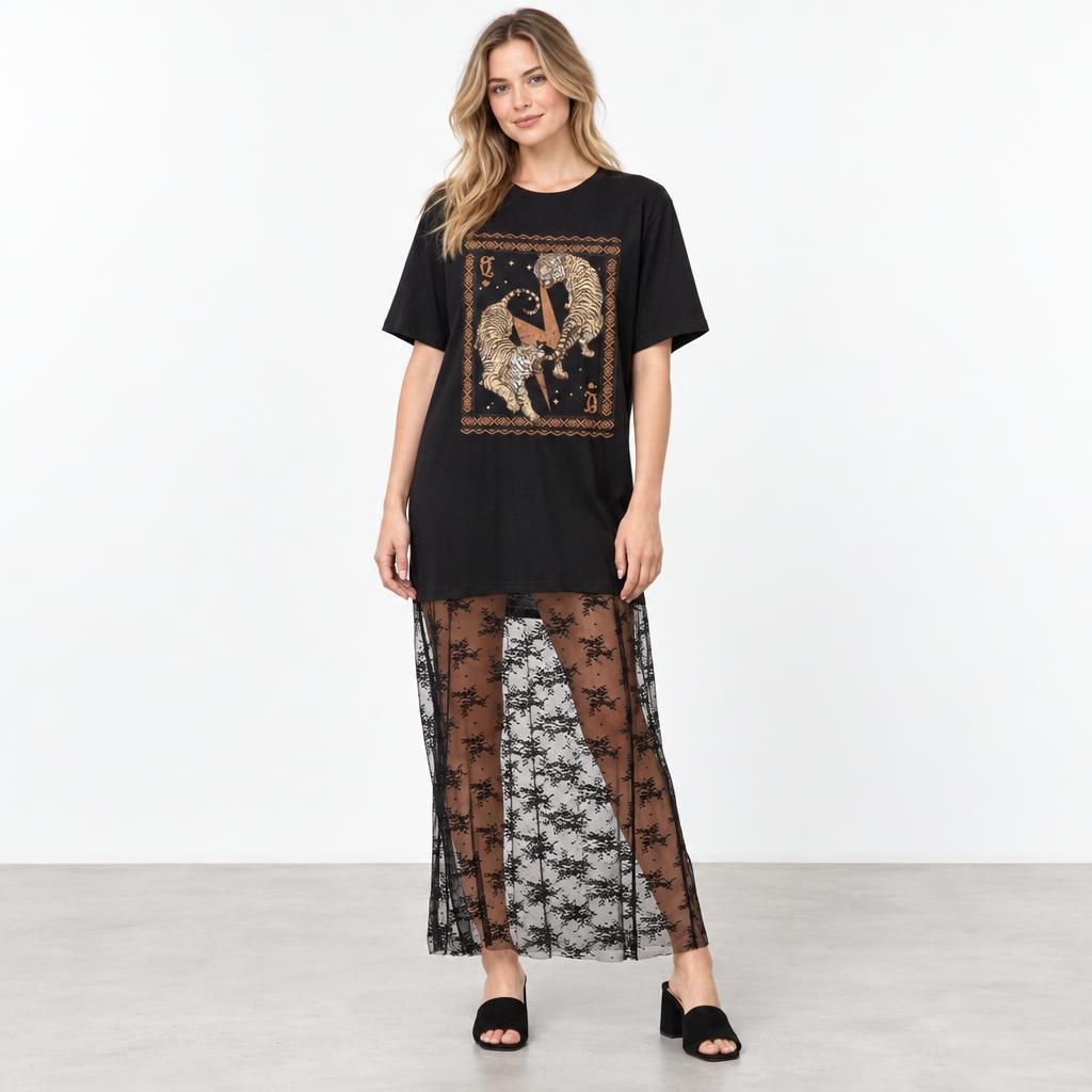 A model wears a black graphic tee, sheer floral skirt, and open-toe heels against a white backdrop.
