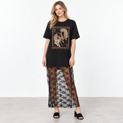 A model wears a black graphic tee, sheer floral skirt, and open-toe heels against a white backdrop.