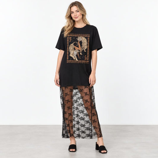 A model wears a black graphic tee, sheer floral skirt, and open-toe heels against a white backdrop.