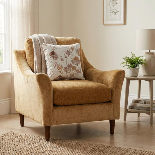 Cozy armchair with floral pillow and throw, beside a lamp and plant on a side table.