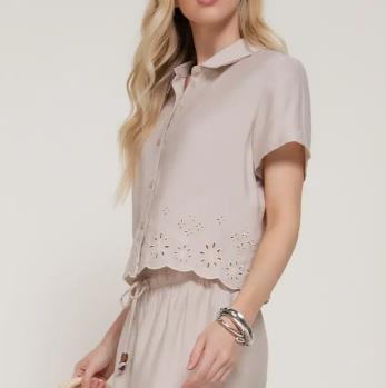 Woman in beige floral top and skirt with wavy hair and bracelets.