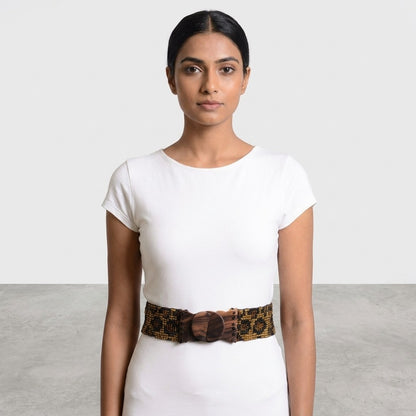 Woman in white dress with patterned belt, neutral background.