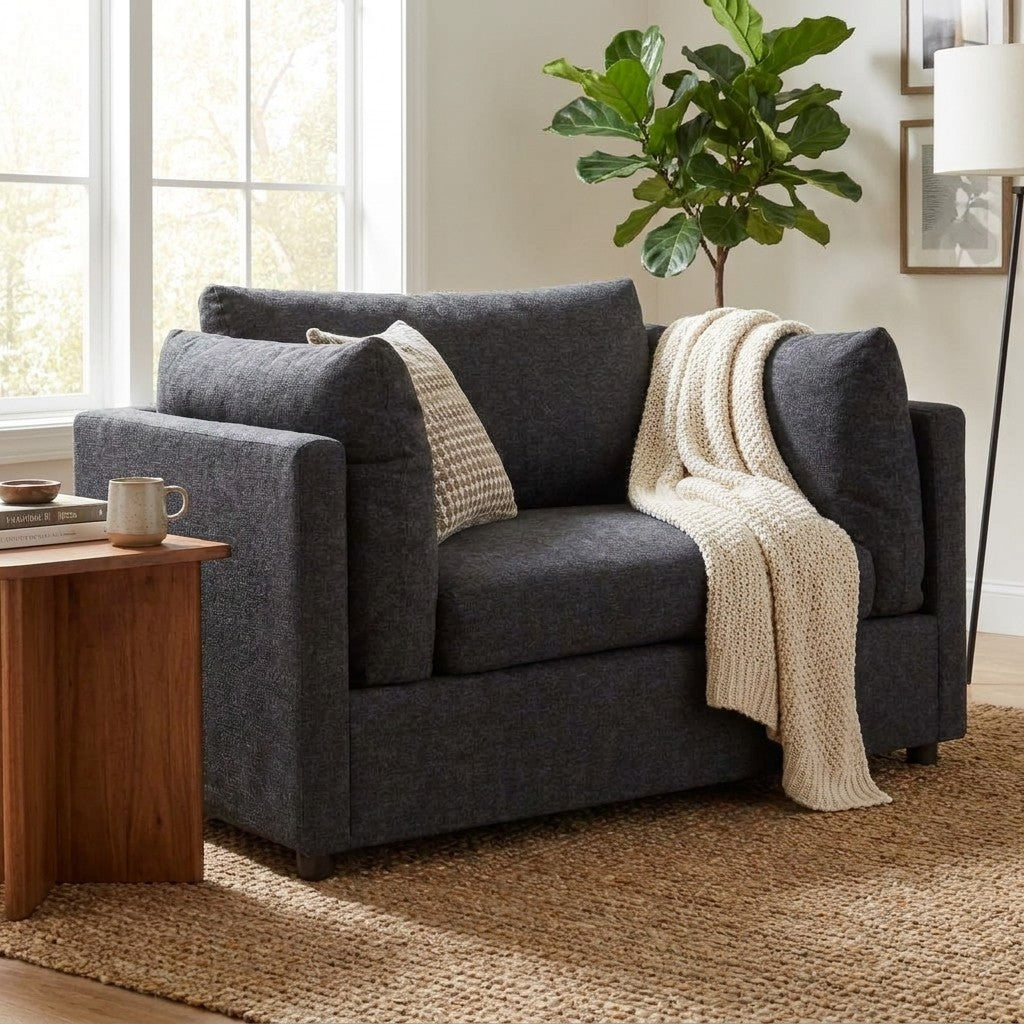 Cozy gray chair, knit blanket, pillow, rug, houseplant, and a window.