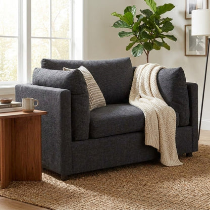 Cozy gray chair, knit blanket, pillow, rug, houseplant, and a window.