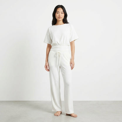 Woman in white lounge set standing barefoot against a plain background.
