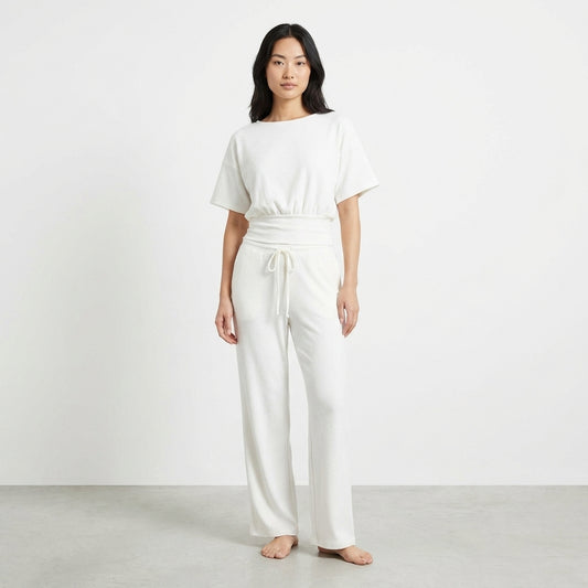 Woman in white lounge set standing barefoot against a plain background.