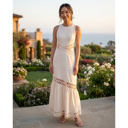Smiling woman in a white dress stands in a garden at sunset.
