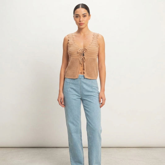Woman in a crochet top and jeans standing against a plain white background.