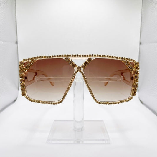 Gold-framed sunglasses with brown lenses on a stand.