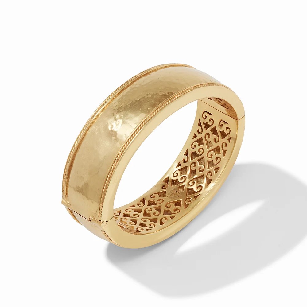 A gold hinged bangle with an engraved filigree interior, displayed on a white background.