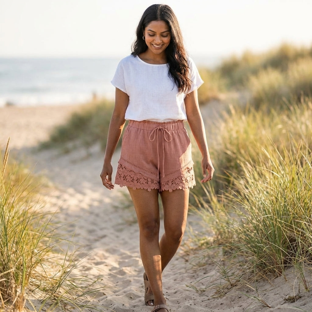 Woman walking on a sandy path by the beach, smiling gently.