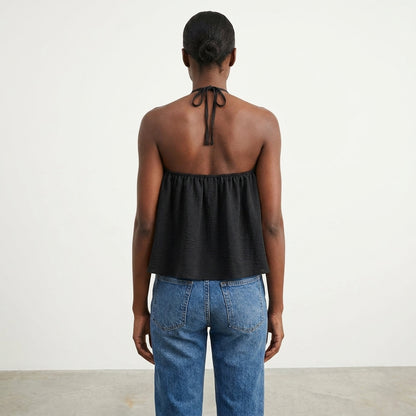 Person in black halter top and jeans, facing away.