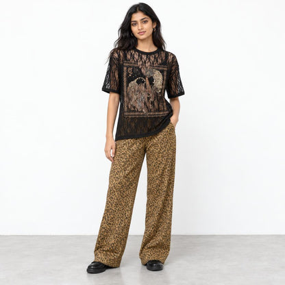 A woman models a black lace graphic top and leopard-print wide-leg pants against a white backdrop.