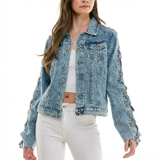 Woman in a denim jacket walks on a sunny, cobblestone path surrounded by plants.