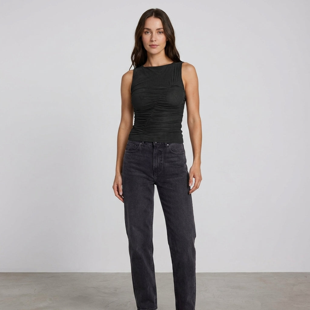 Woman posing in dark top and jeans against a plain background.