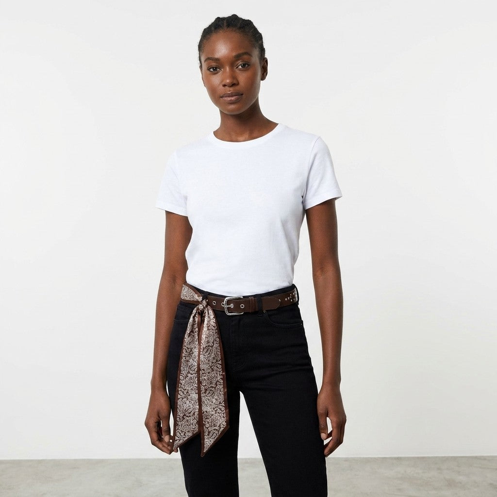 Woman in a white shirt and black jeans stands against a plain background.