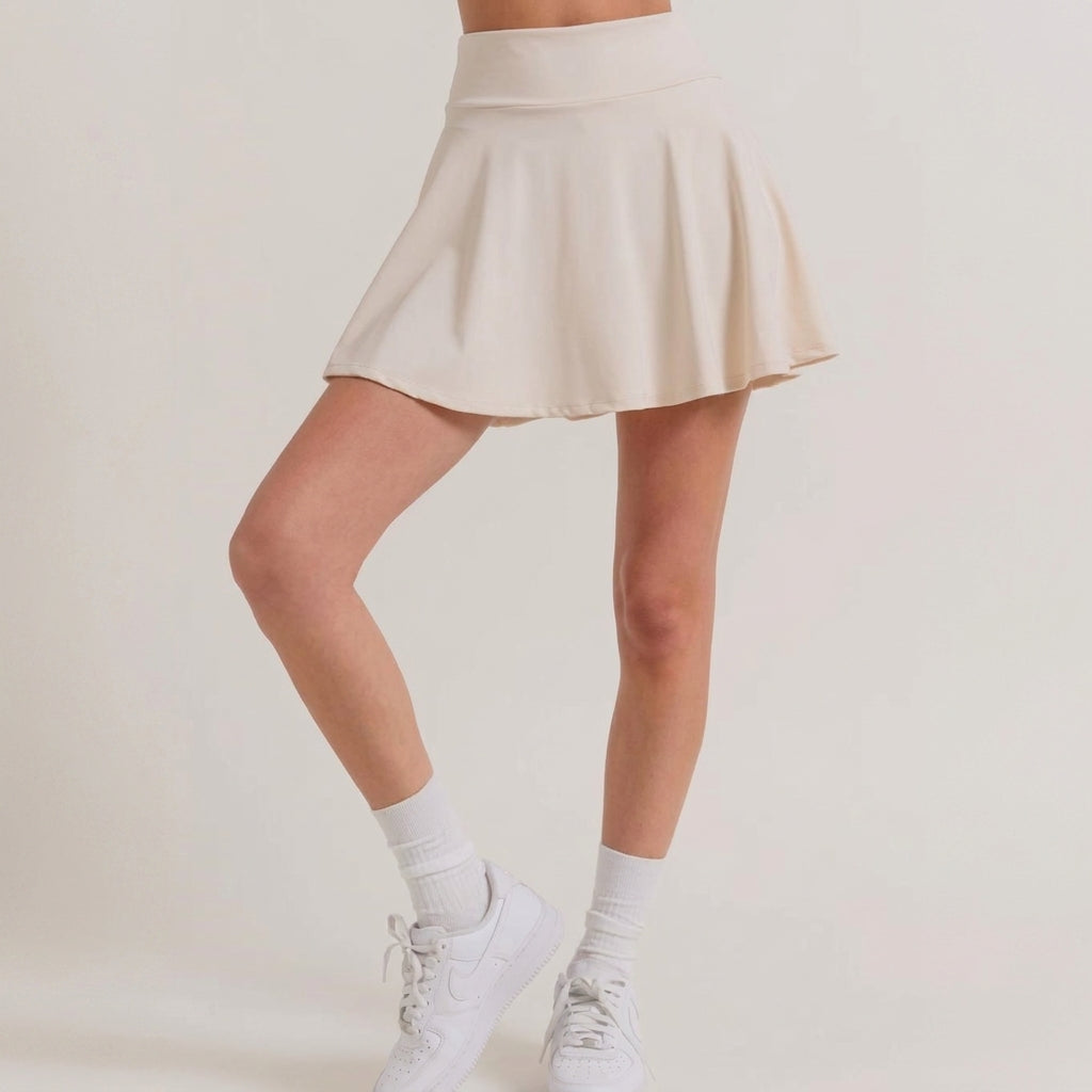 Woman in a beige skirt with white sneakers and socks, standing gracefully.