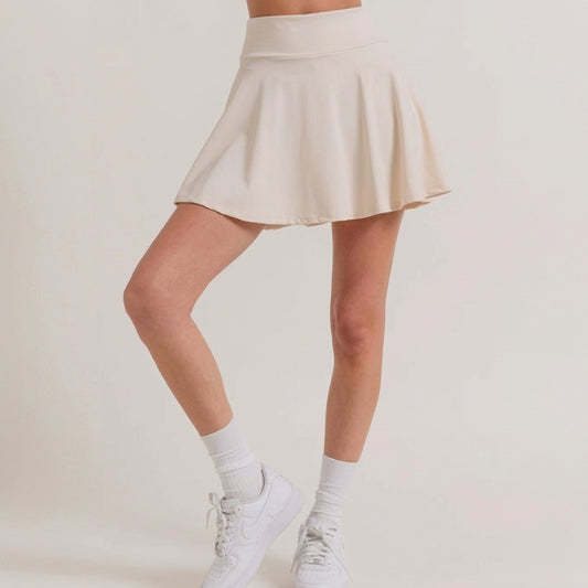 Woman in a beige skirt with white sneakers and socks, standing gracefully.