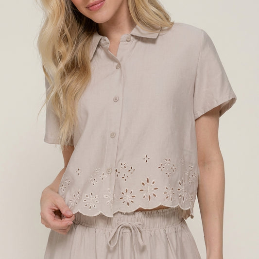 Woman in beige embroidered blouse holding the hem.