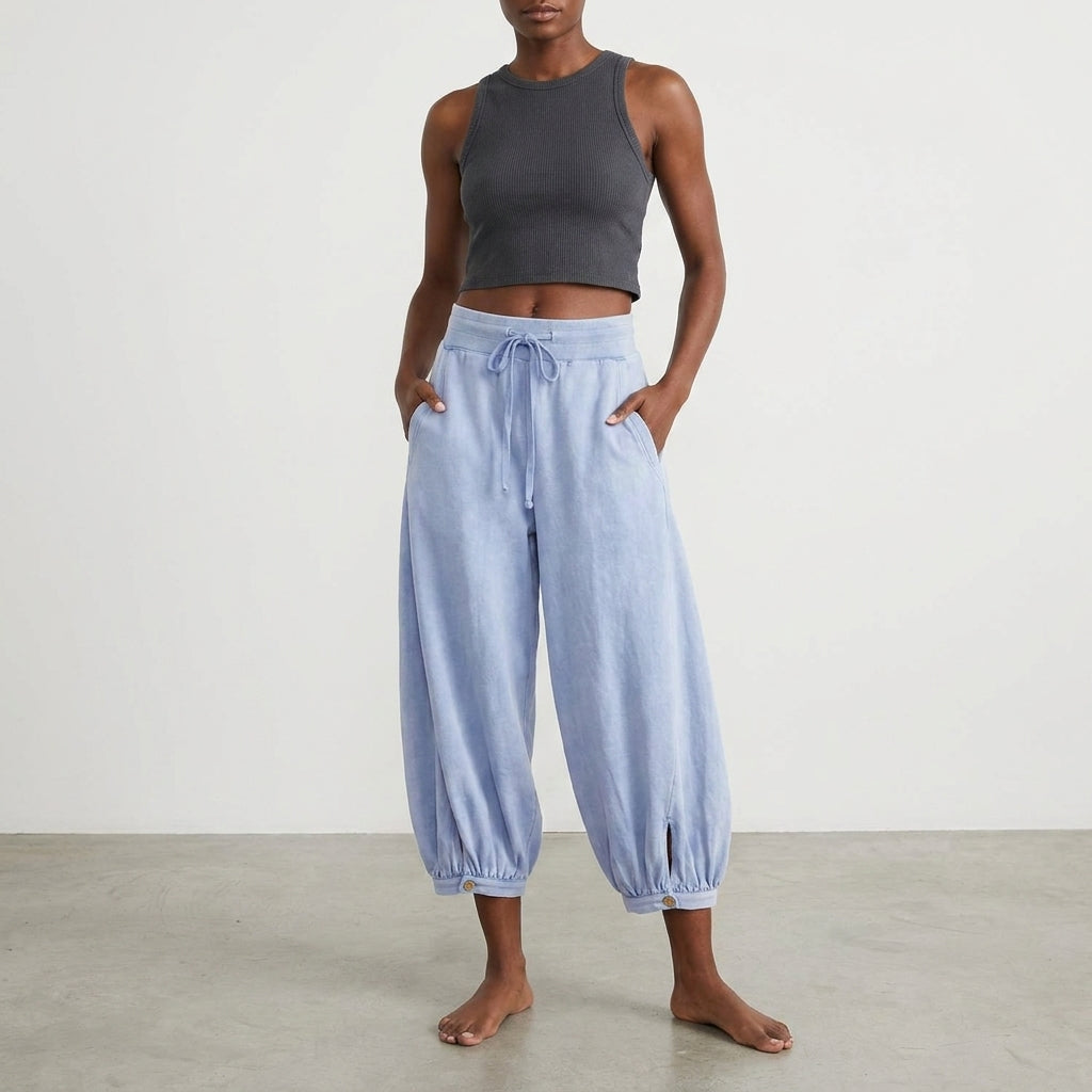 Person in a black crop top and loose blue pants standing barefoot.