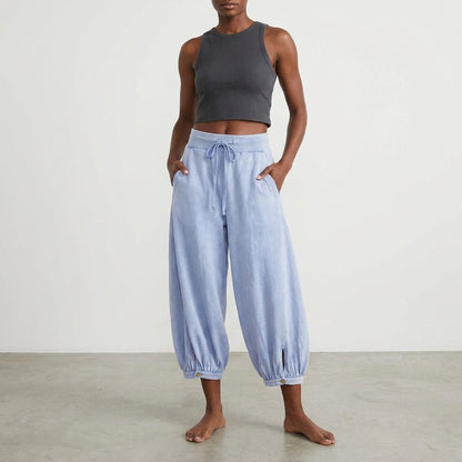 Person in a black crop top and loose blue pants standing barefoot.