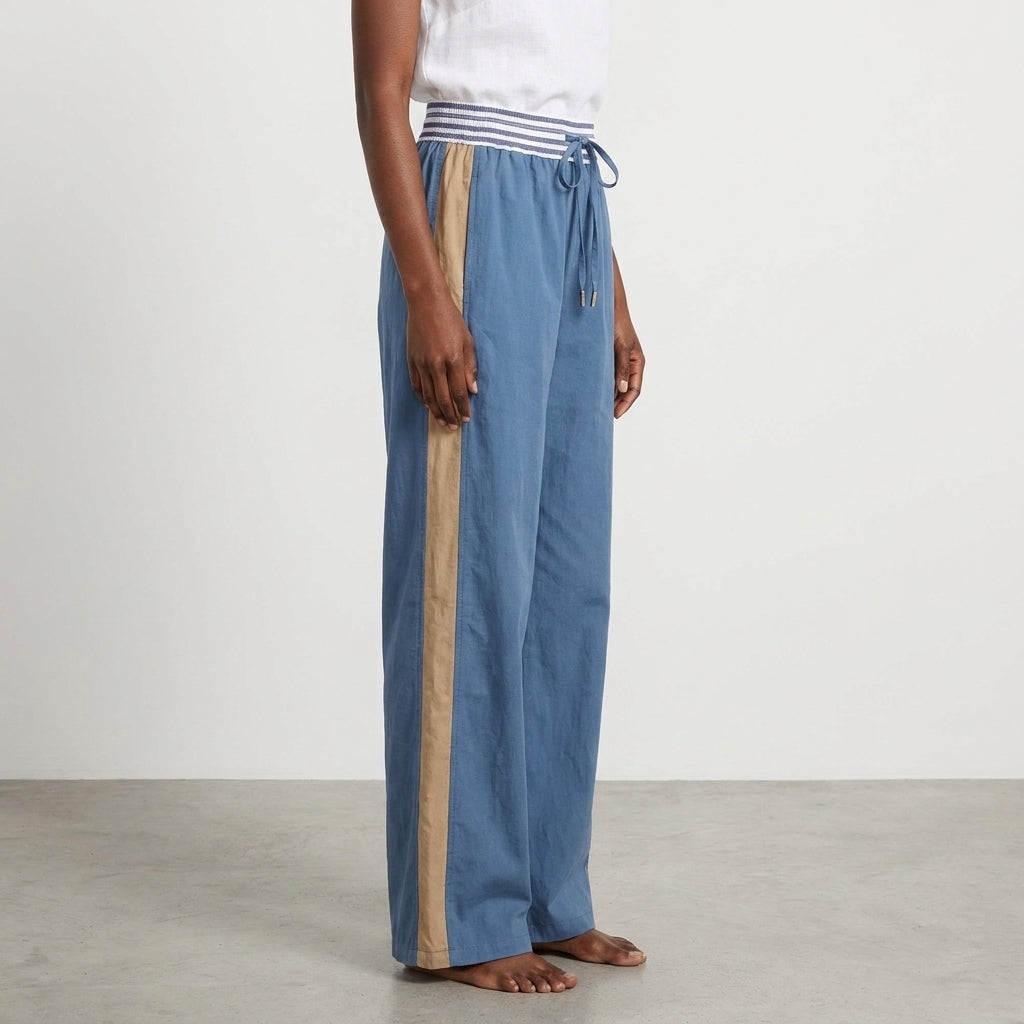 Person wearing blue pants with beige stripe and white top, barefoot on gray floor.