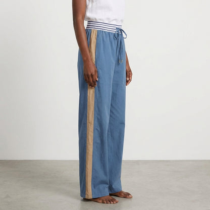 Person wearing blue pants with beige stripe and white top, barefoot on gray floor.