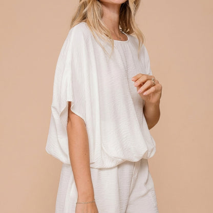 Person wearing a loose, white outfit against a beige background.