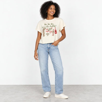 A smiling woman models a festive graphic T-shirt with light-wash jeans and white sneakers.