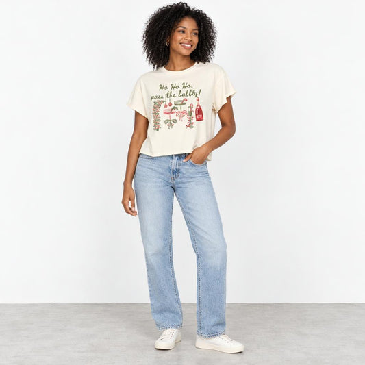 A smiling woman models a festive graphic T-shirt with light-wash jeans and white sneakers.