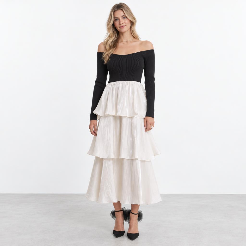 A woman models a black off-shoulder top with a flowing, tiered white skirt.