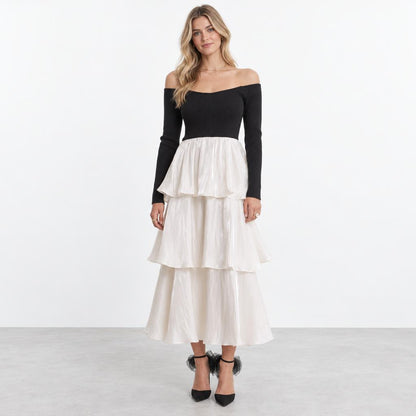 A woman models a black off-shoulder top with a flowing, tiered white skirt.