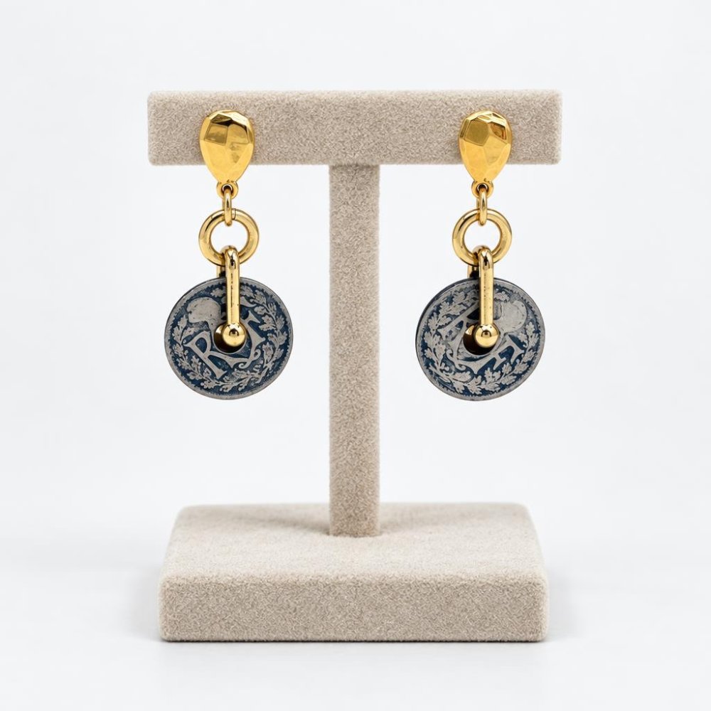 Gold-tone drop earrings with ornate blue and silver circular pendants on a display stand.