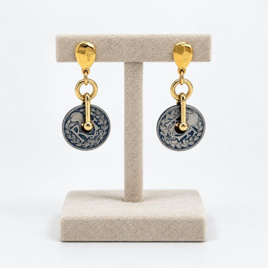 Gold-tone drop earrings with ornate blue and silver circular pendants on a display stand.