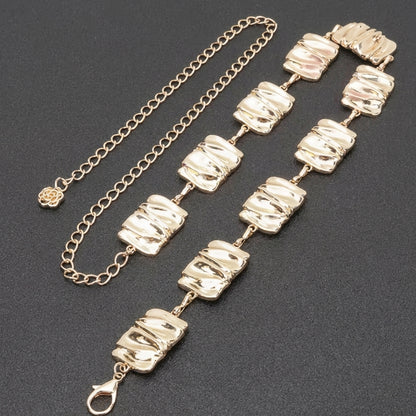 Gold chain bracelet with textured square links on a dark background.