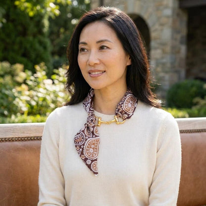 A woman in a cream sweater and patterned scarf smiles outdoors in the sunlight.