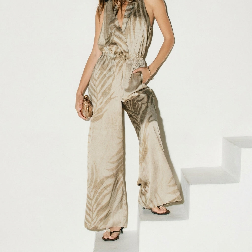Person in a flowy, patterned jumpsuit on white steps, holding a clutch.