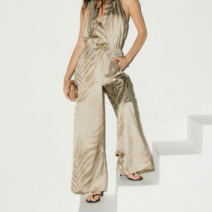 Person in a flowy, patterned jumpsuit on white steps, holding a clutch.
