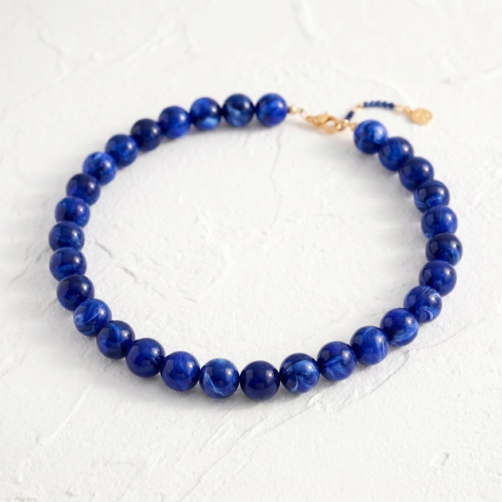 Blue bead necklace with gold clasp on white textured background.