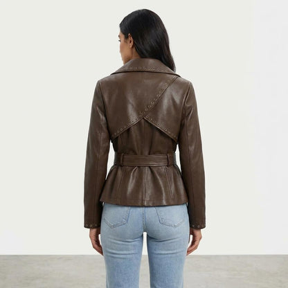 A woman models a belted brown leather jacket with decorative eyelet detailing and light blue jeans.
