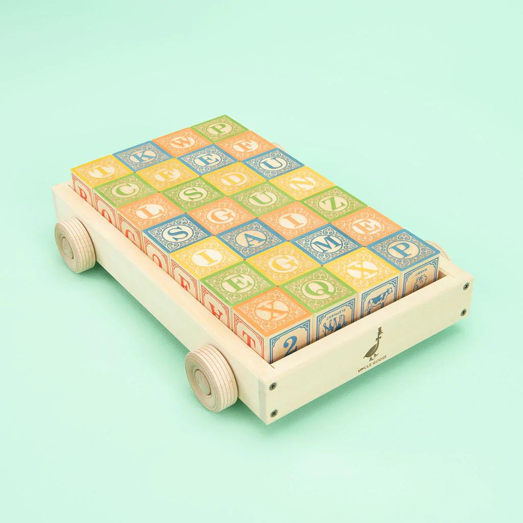 Wooden cart with colorful alphabet blocks on a mint background.