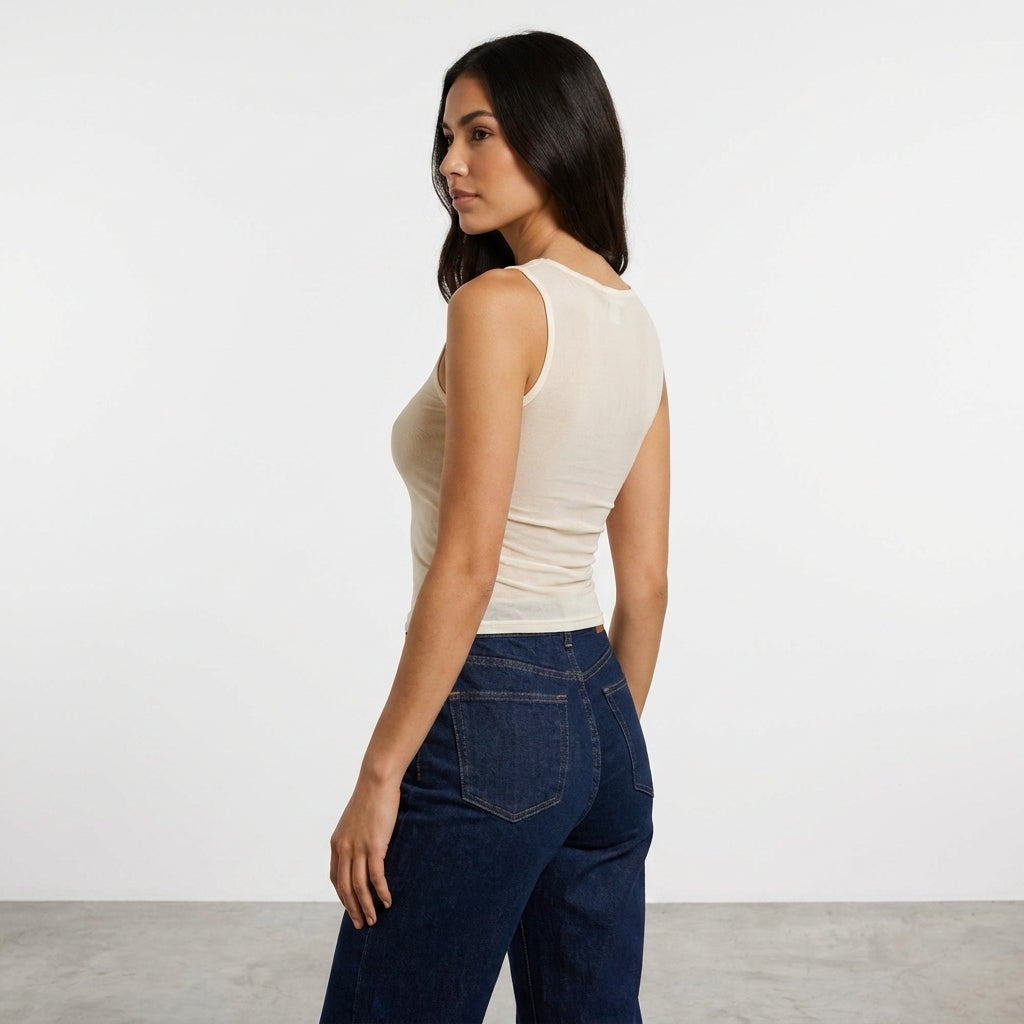 Woman in a sleeveless top and jeans, posing side view.